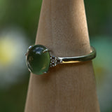 925 silver ring with a green gemstone on a wooden stand against a blurred natural background
