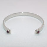 silver open bangle featuring a Garnet at each end