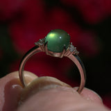 vintage silver ring with a green gemstone held in a hand against a blurred red background