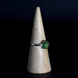 Vintage solid silver ring with a green gemstone on a wooden cone against a black background