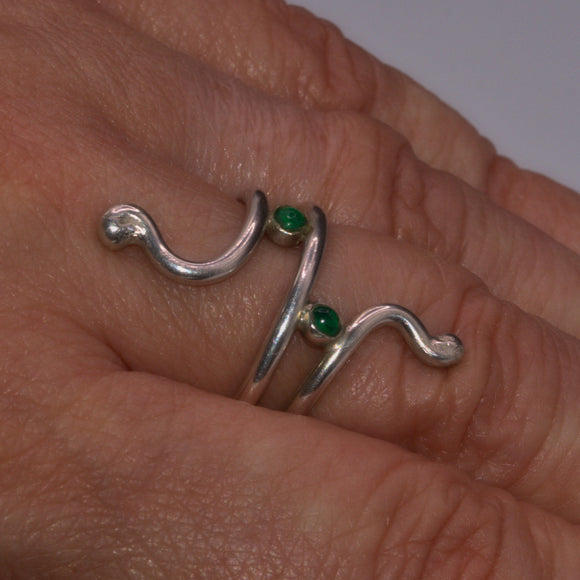 Solid silver ring with green Onyx gemstones on a person's finger against a neutral background