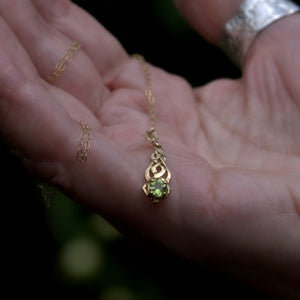 Solid 9ct gold necklace with a green gemstone Celtic pendant held in a hand against a blurred background