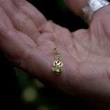 Solid 9ct gold necklace with a green gemstone Celtic pendant held in a hand against a blurred background