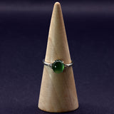 Ring with a green gemstone on a wooden cone against a dark background