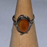 Silver ring with an amber stone on a wooden stand against a gray background