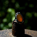 Solid silver ring with an Amber stone on a dark surface with a blurred green background