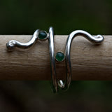 Solid sterling silver ring with green gemstones on a wooden stick against a dark background