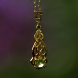 Solid 9ct yellow gold Celtic pendant with a green Peridot gemstone on a blurred background